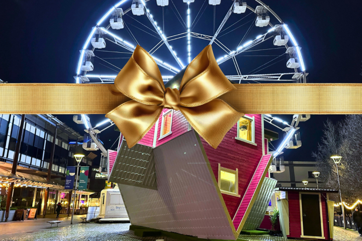 Upside-down house at night with Ferris wheel in background, overlaid with a gold ribbon and bow.