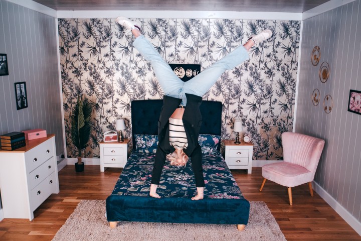 Person doing a handstand on a bed in a stylishly decorated bedroom.
