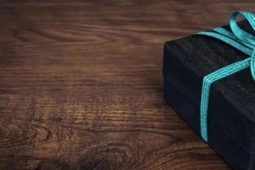 Dark gift box with turquoise ribbon on wooden surface.
