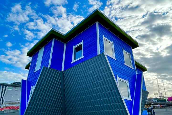 Upside-down blue house under a cloudy sky.
