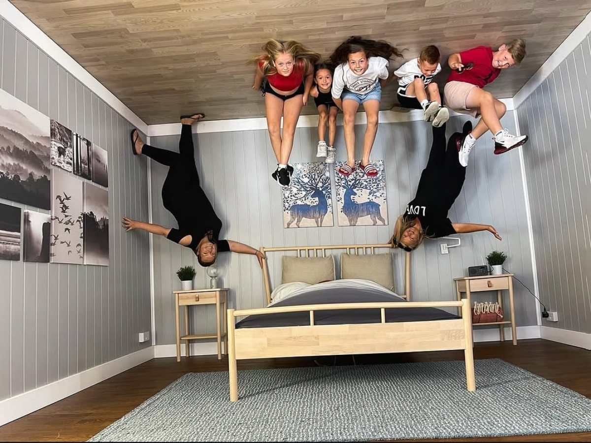 People posing as if standing on a ceiling in a bedroom setup.